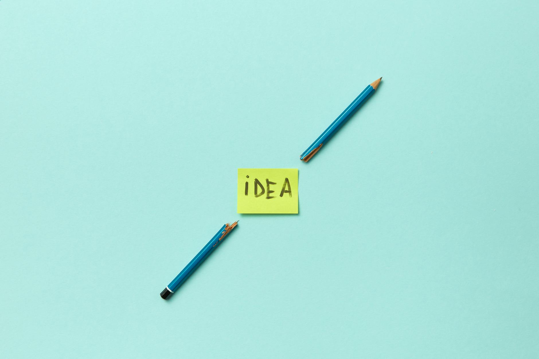 a word idea written on a sticky note placed between broken pencils